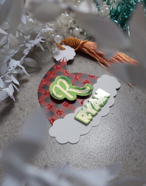 Christmas tag in the shape of a hat witha gold tassle and the name Ryan on it.