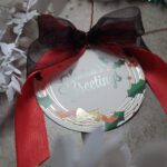 Circular Christmas tag with Seasons Greeting foiled in gold and a red and black ribbon tied to it.